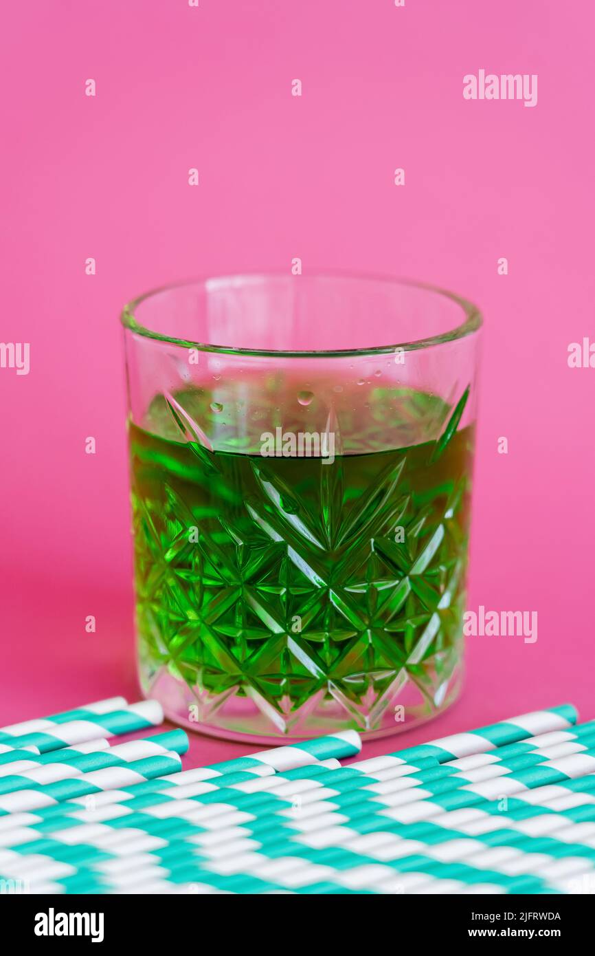 striped paper straws near faceted glass with green cocktail on pink Stock Photo