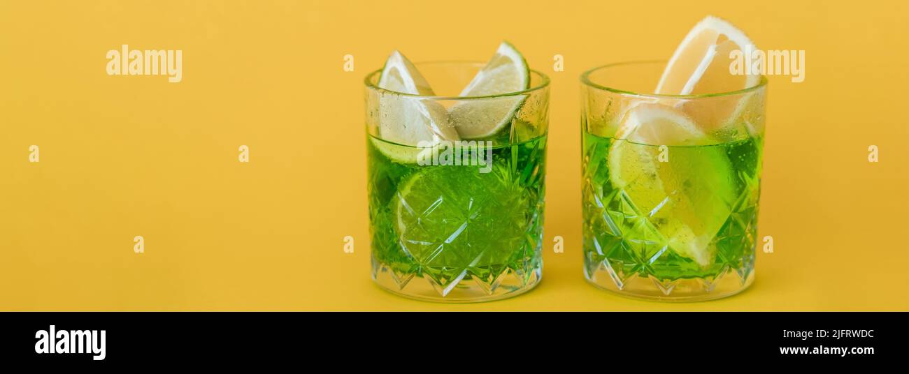 sliced citrus fruits in glasses with sparkling mojito drink on yellow, banner Stock Photo