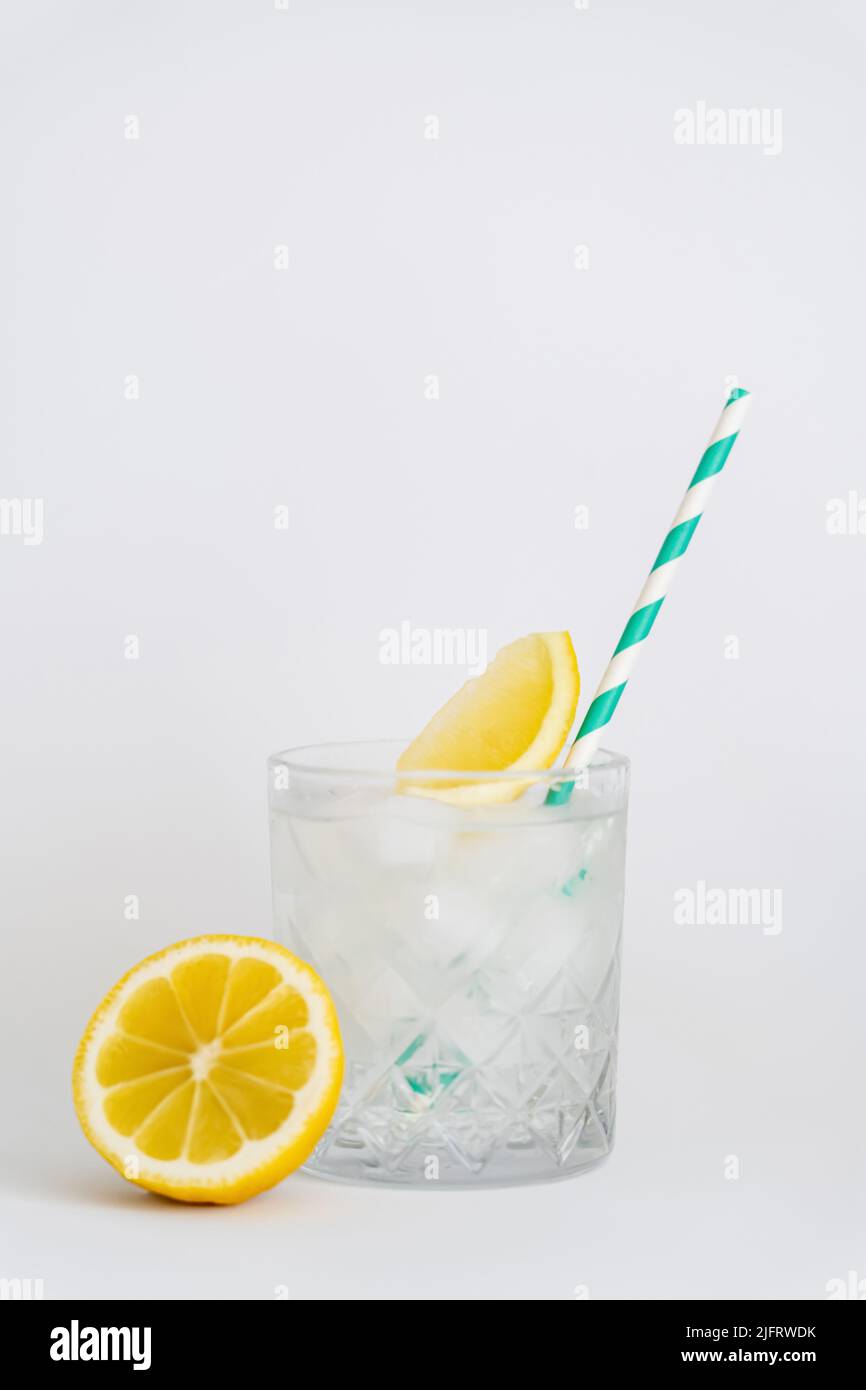 faceted cold glass with ice cubes, paper straw and sliced lemons on white Stock Photo