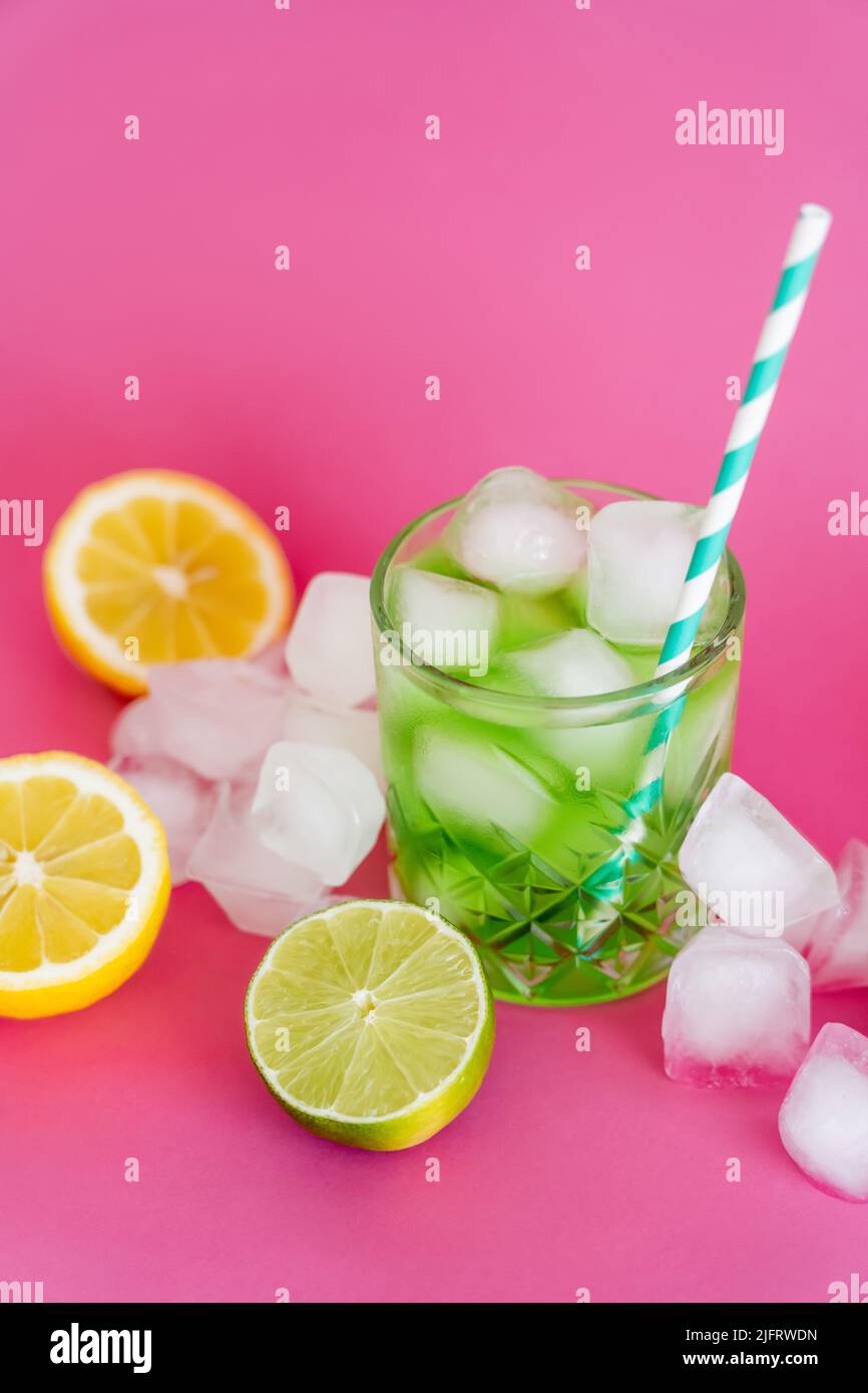 ice cubes in glass with mojito drink and straw near citrus fruits on pink Stock Photo