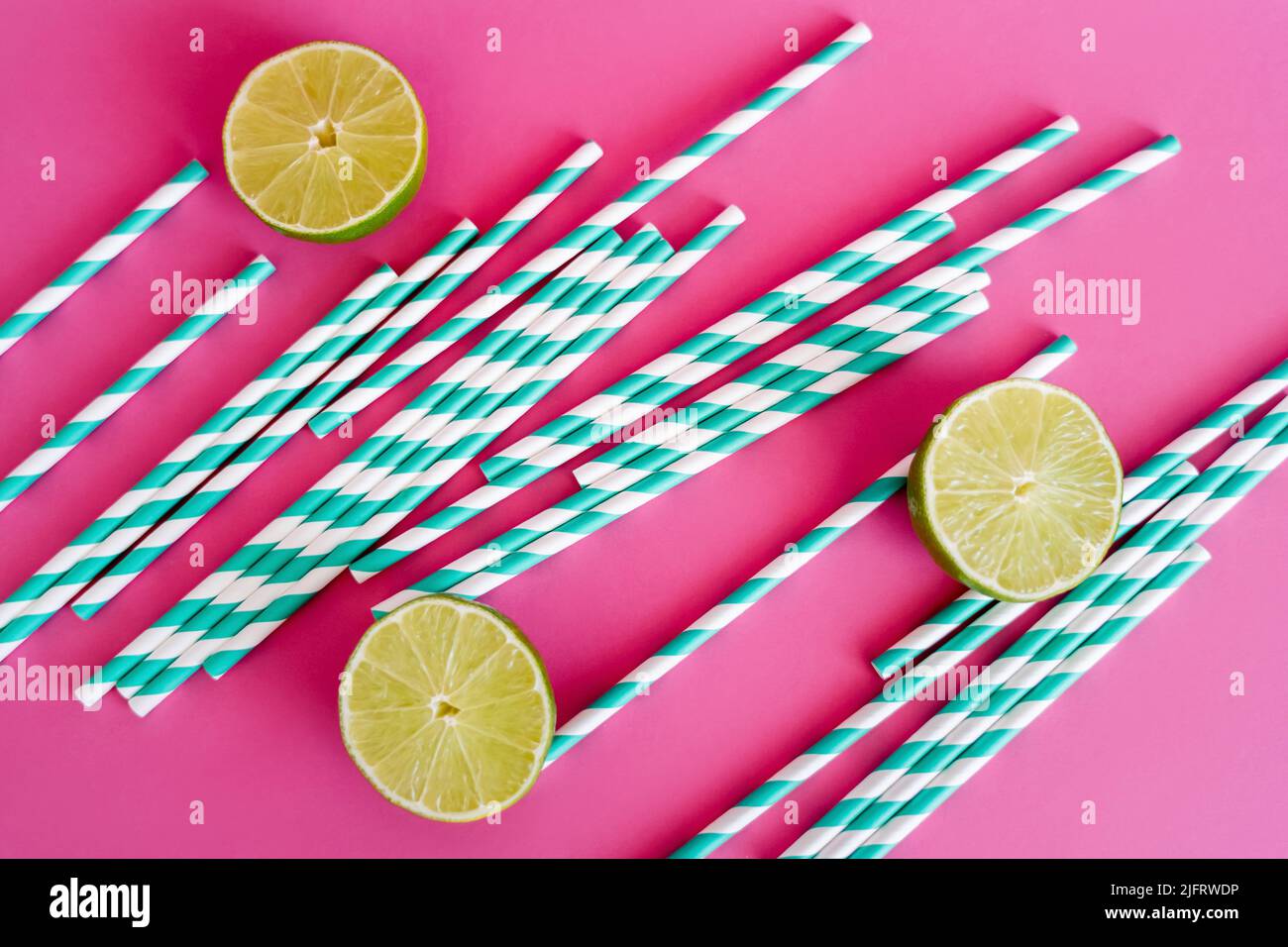 top view of striped blue and white straws near limes on pink background Stock Photo