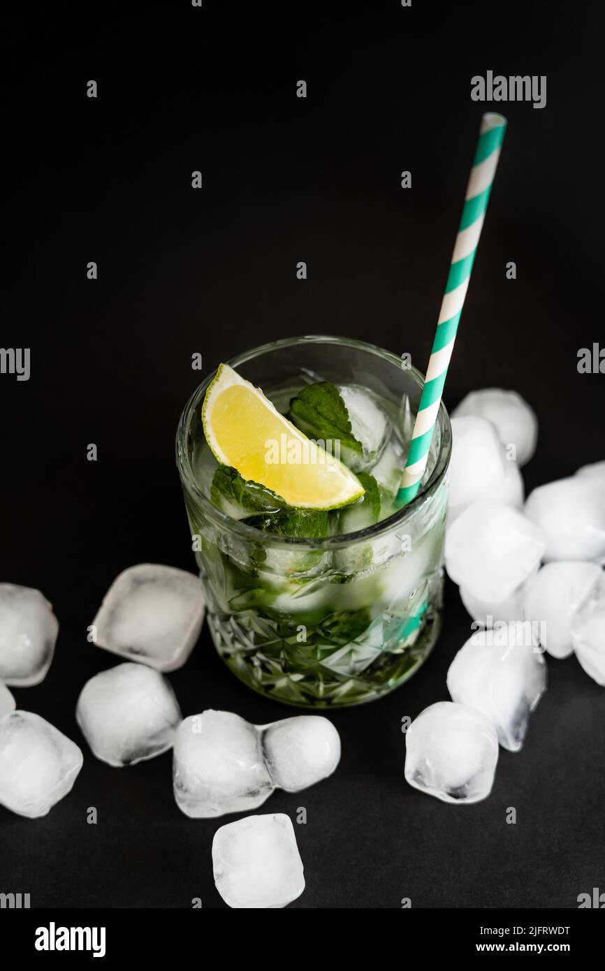 high angle view of cool faceted glass with mojito near ice cubes on black Stock Photo