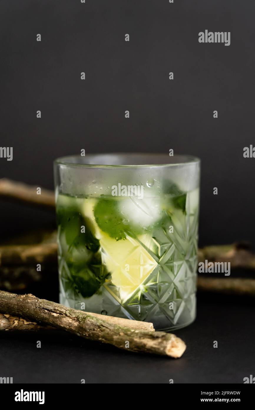 faceted cold glass with melting ice cubes and sliced lime near wooden sticks on black Stock Photo