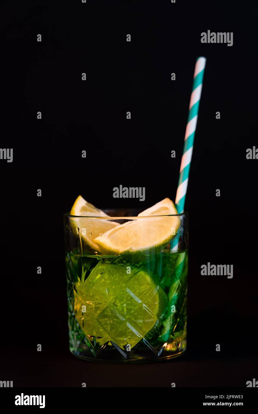 sliced citrus fruits in glass with alcohol drink and straw isolated on black Stock Photo