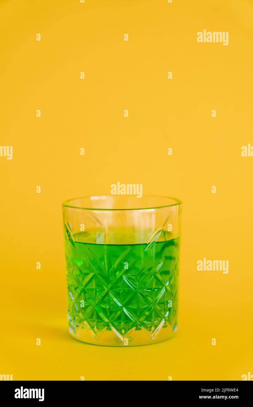 faceted glass with green alcohol drink on yellow Stock Photo