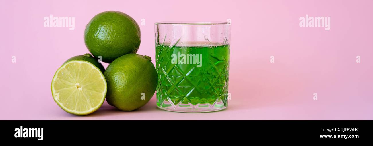 green alcohol drink in glass near fresh and organic limes on pink, banner Stock Photo