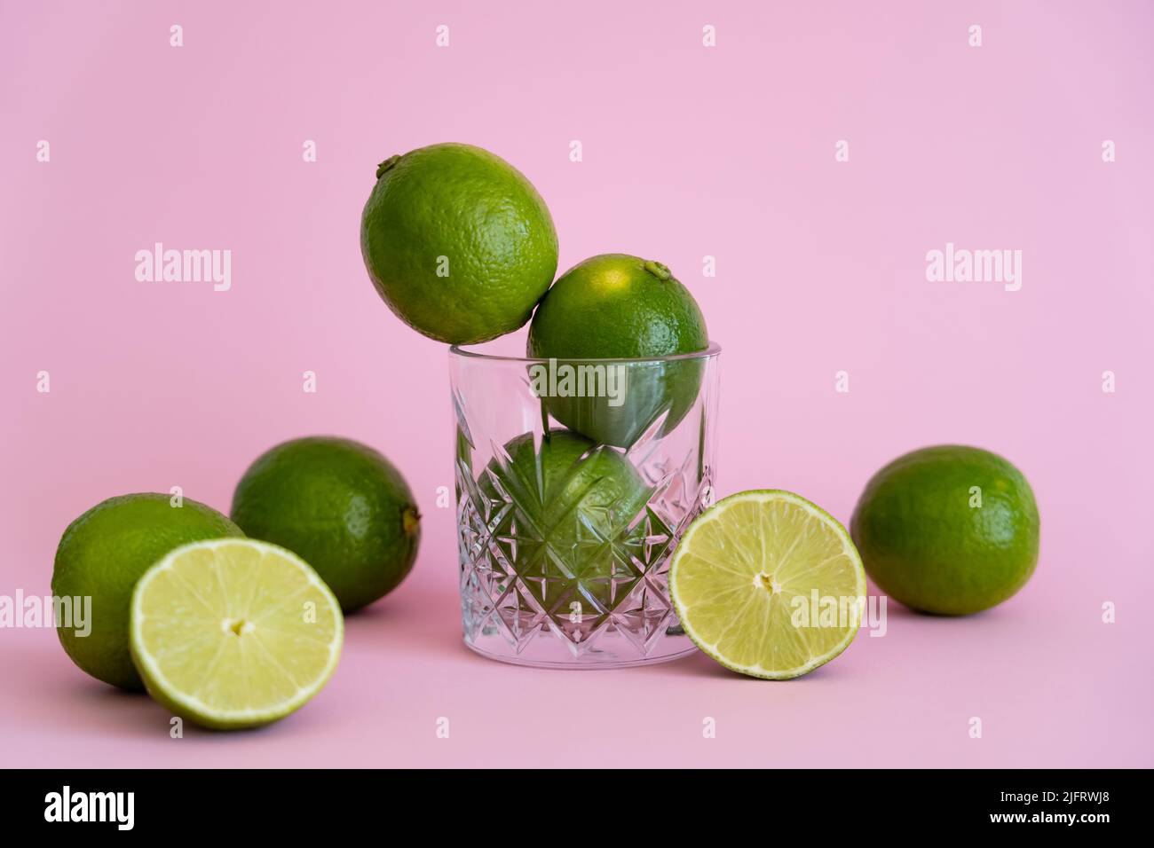 green fresh citrus fruit in faceted glass near halves of limes on pink background Stock Photo