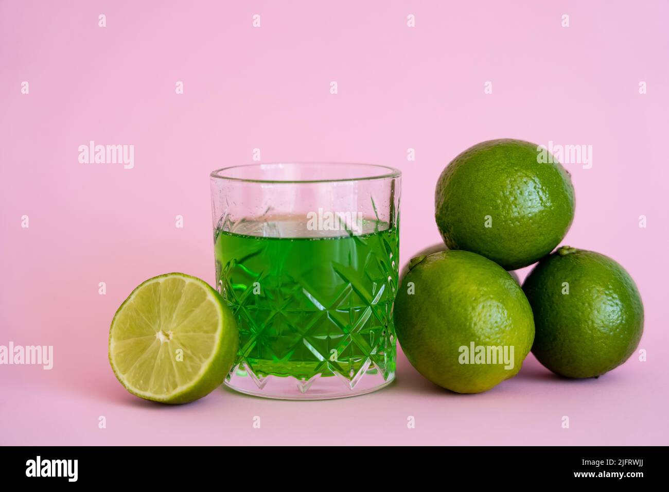 green fresh limes near alcohol drink in faceted glass on pink Stock Photo
