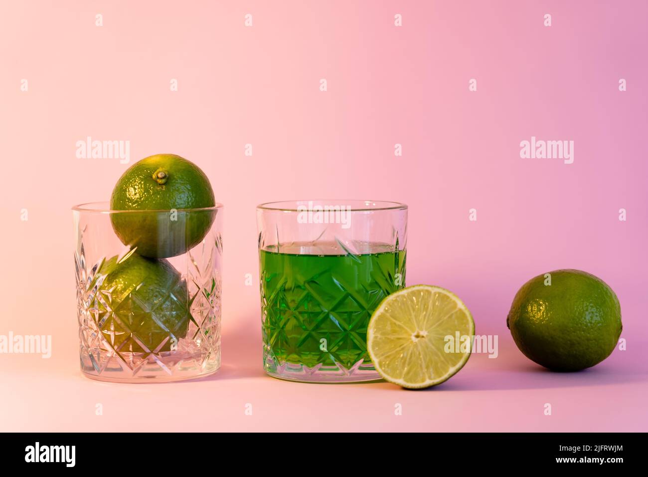 green alcohol drink near faceted glass with fresh limes on pink background Stock Photo