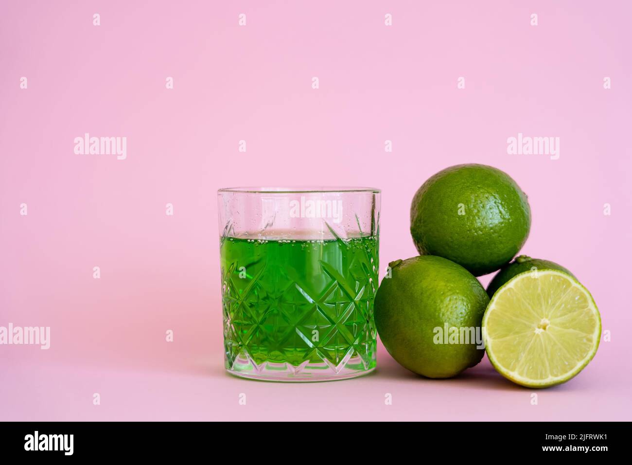 green alcohol drink in glass near fresh and organic limes on pink Stock Photo