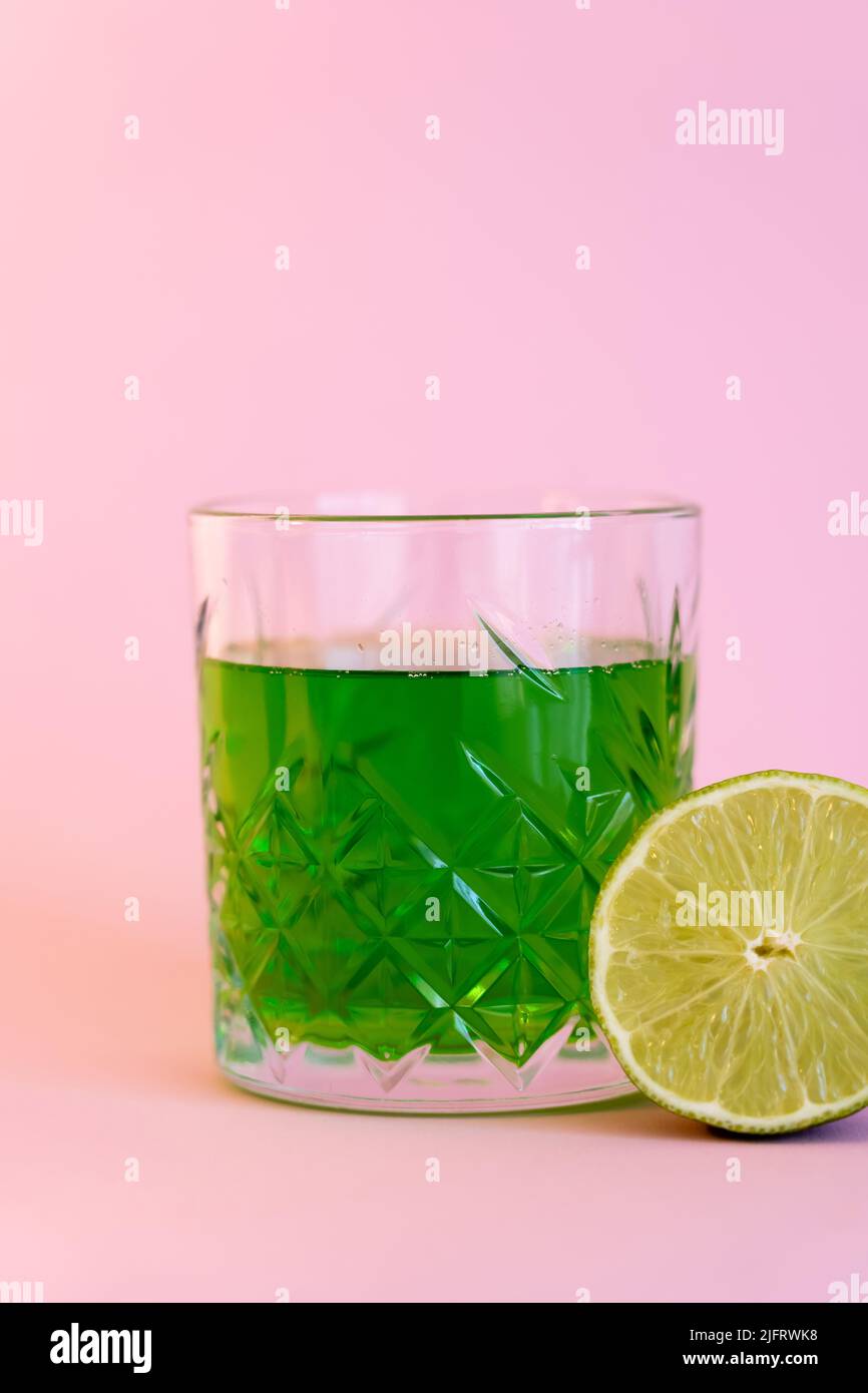green alcohol drink in glass near half of fresh lime on pink Stock Photo