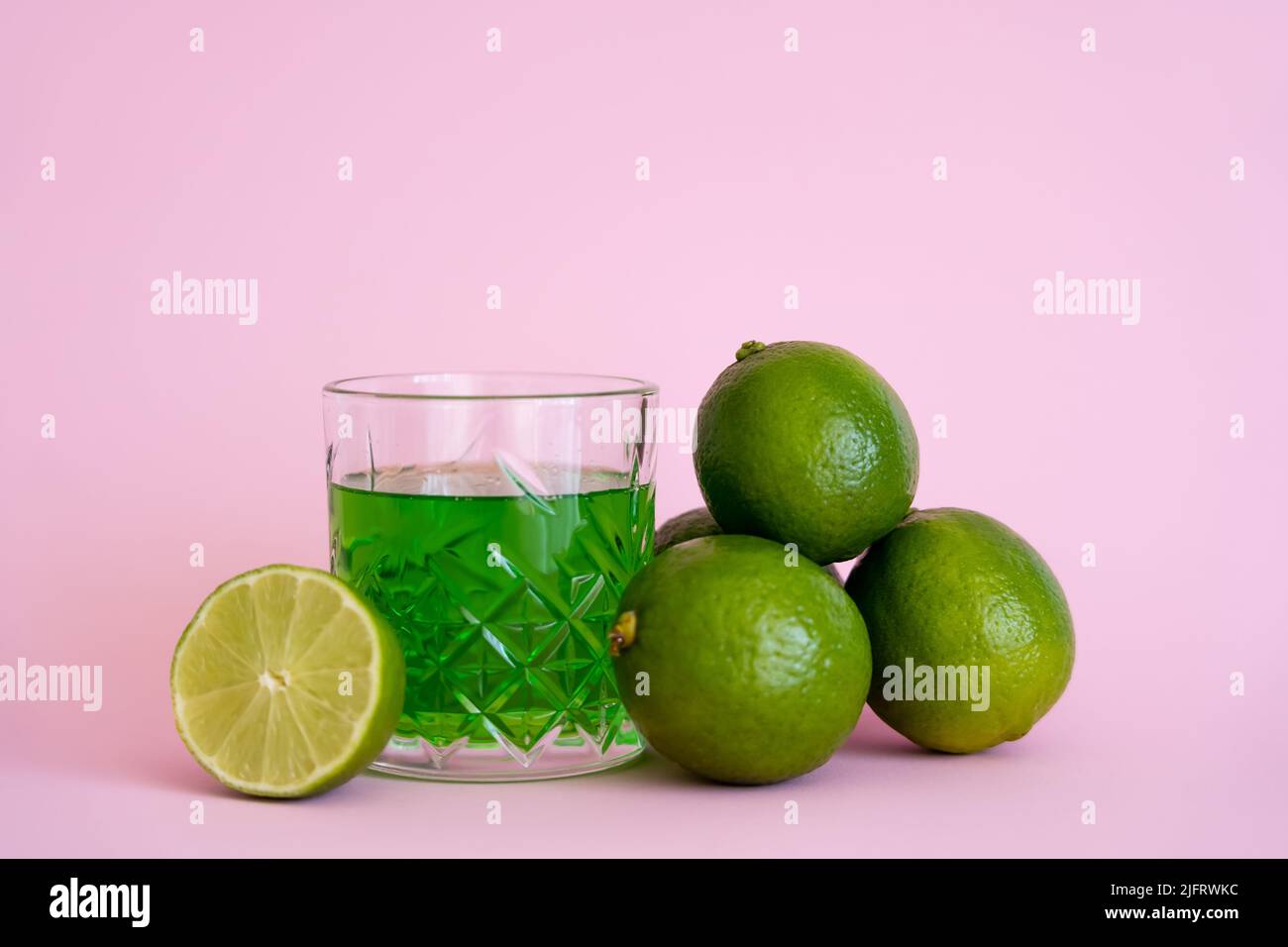 green liquid in glass near fresh limes on pink background Stock Photo