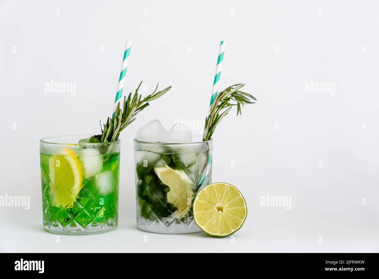 cool faceted glasses with cocktails and ice cubes near citrus fruits on white Stock Photo