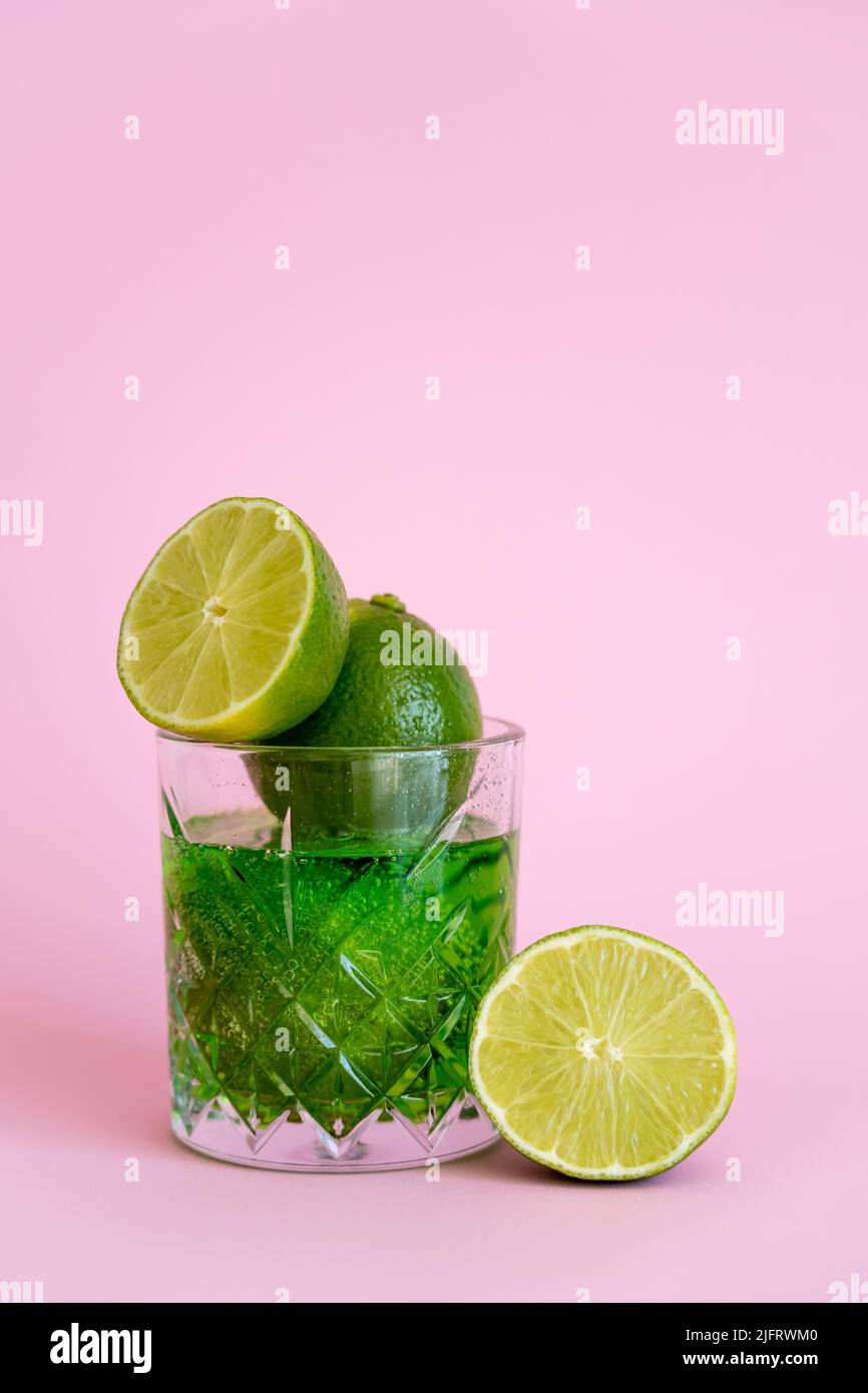 green and fresh limes in faceted glass with sparkling alcohol drink on pink Stock Photo