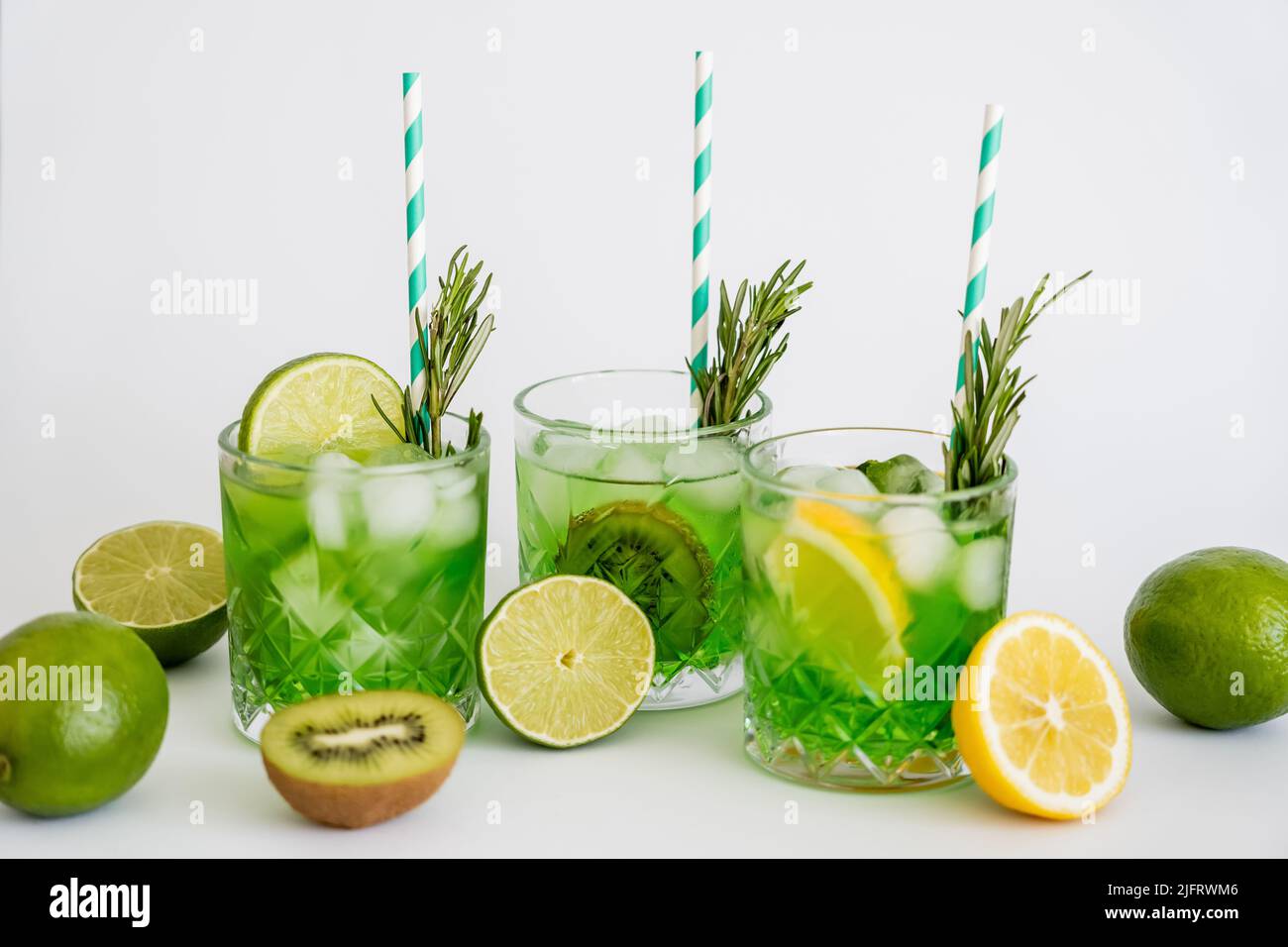 faceted glasses with cold green cocktail, straws and fruits on white Stock Photo