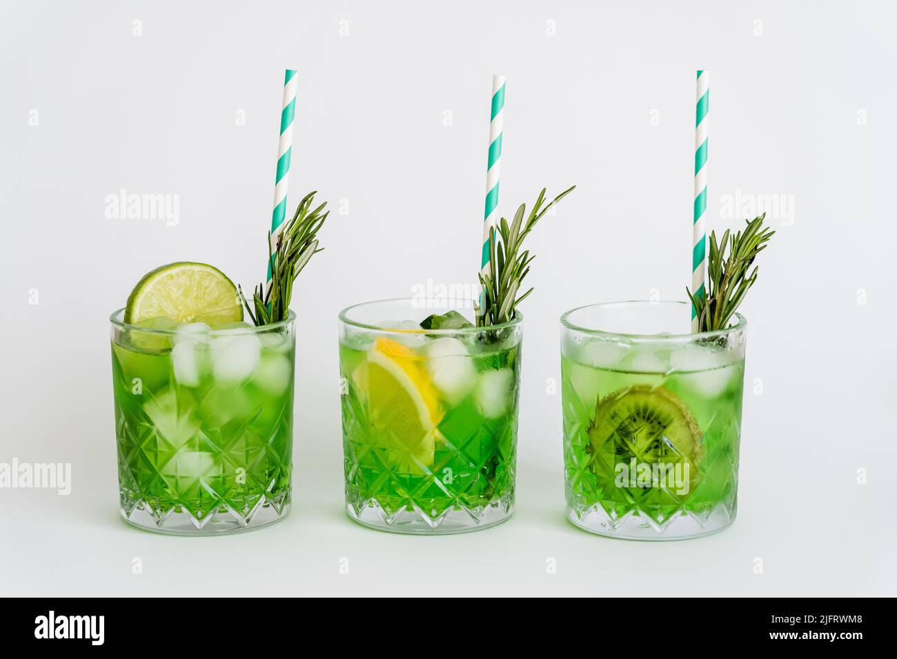 faceted glasses with green cocktail, ice cubes and fruits on white Stock Photo