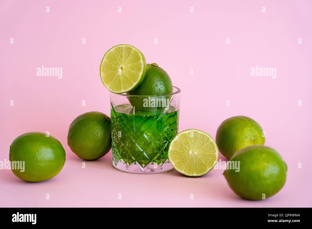 green and fresh limes in faceted glass with alcohol drink on pink Stock Photo