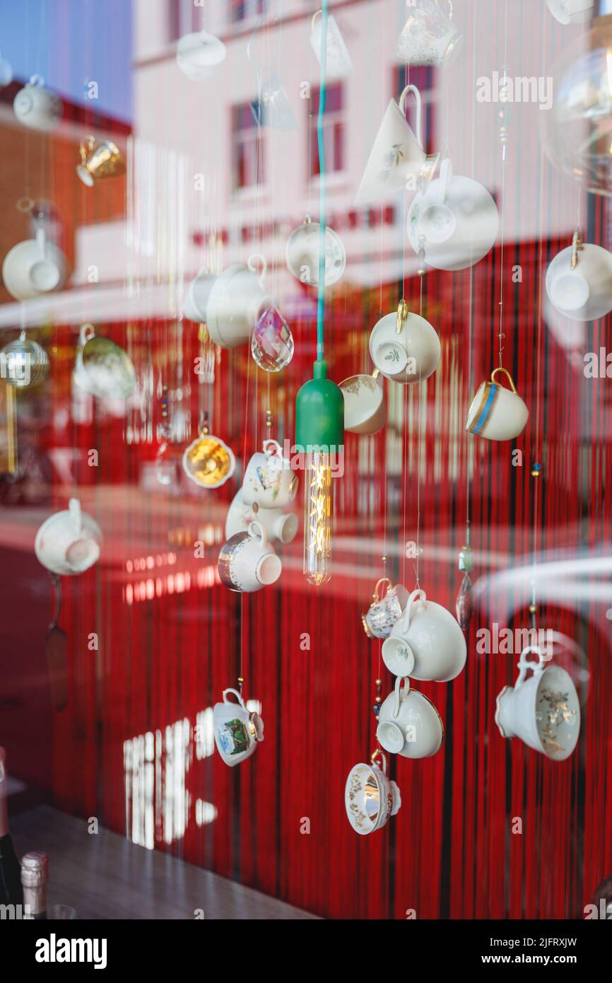 a shop window with the reflection of other buildings on the street. The window dressing is hanging teacups and light bulbs. Stock Photo