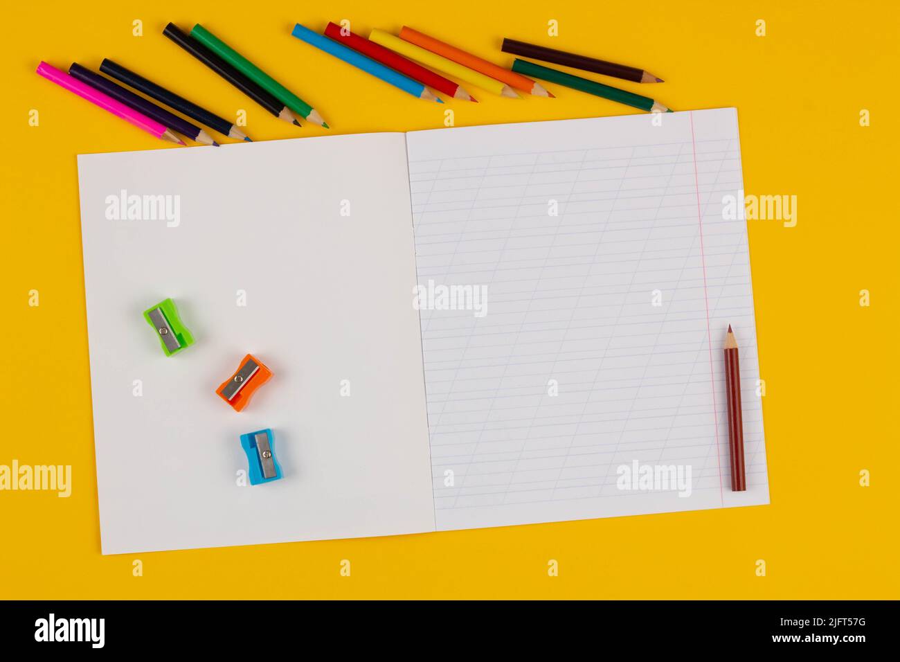 School notebook on a yellow background with copy space text, colorful pencils, pencil sharpeners. Back to school. Blank sheet of paper with oblique Stock Photo