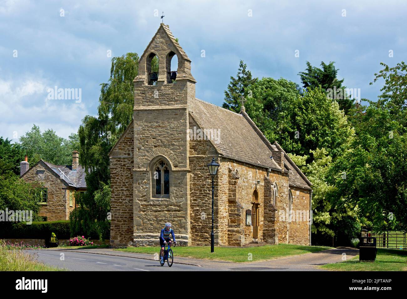 Man cycling past All Saints Church in the village of Sutton Bassett, Northamptonshire, England UK Stock Photo