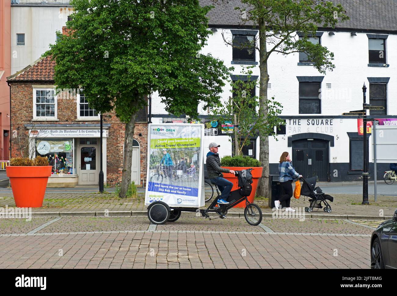 Man riding bicycle, with sign promoting the benefits of travelling by bike, Selby,North Yorkshire, England UK Stock Photo