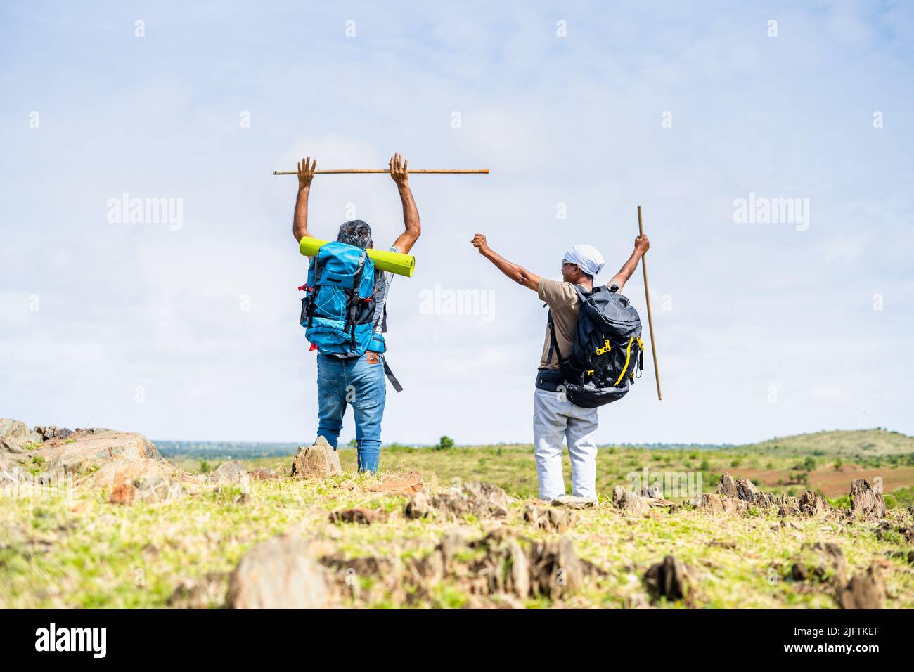 Back view shot of hikers celebration by raising hands with stick on top
