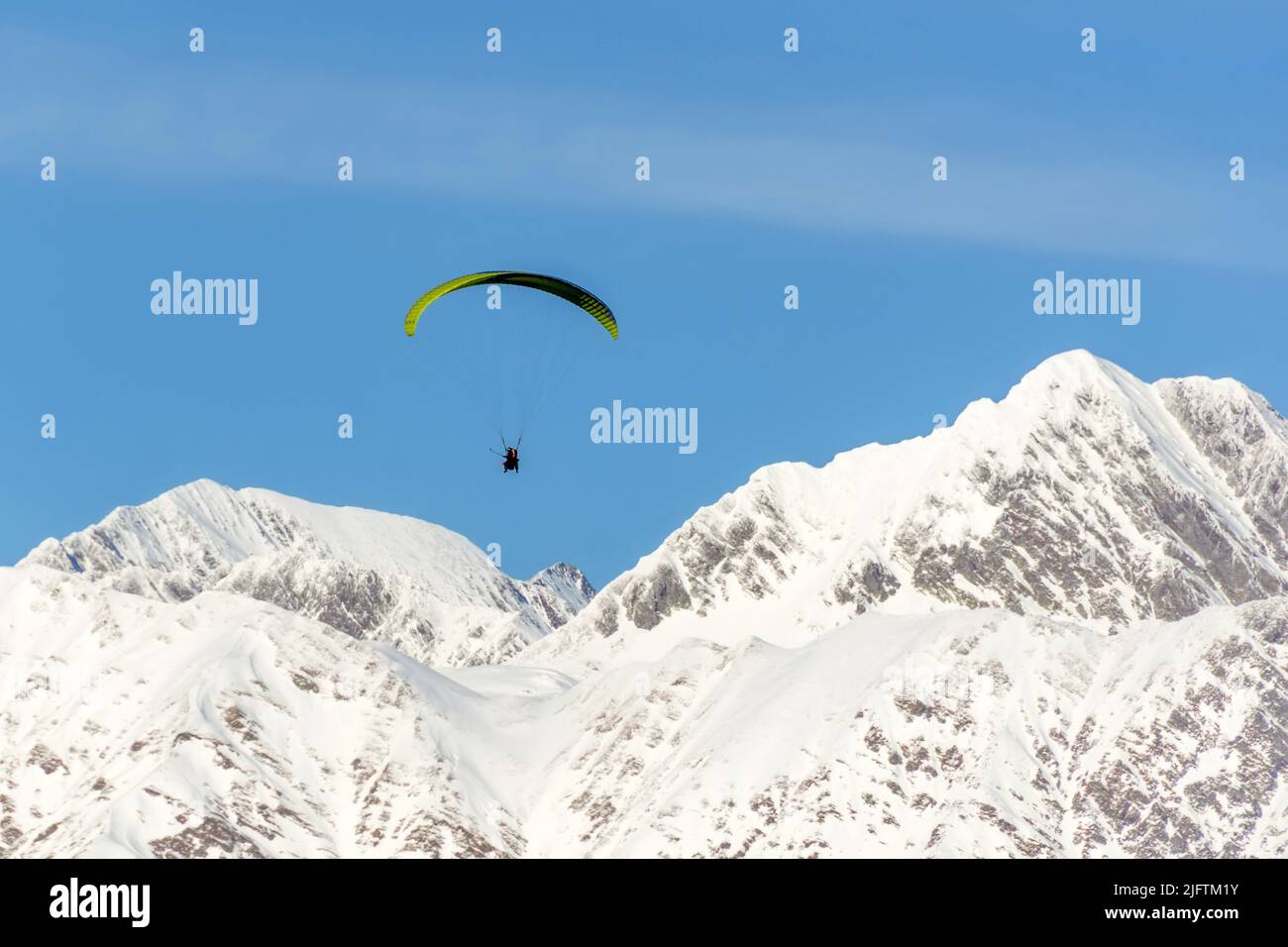 Paraglide flying flies over the snow-capped mountains valley Stock Photo