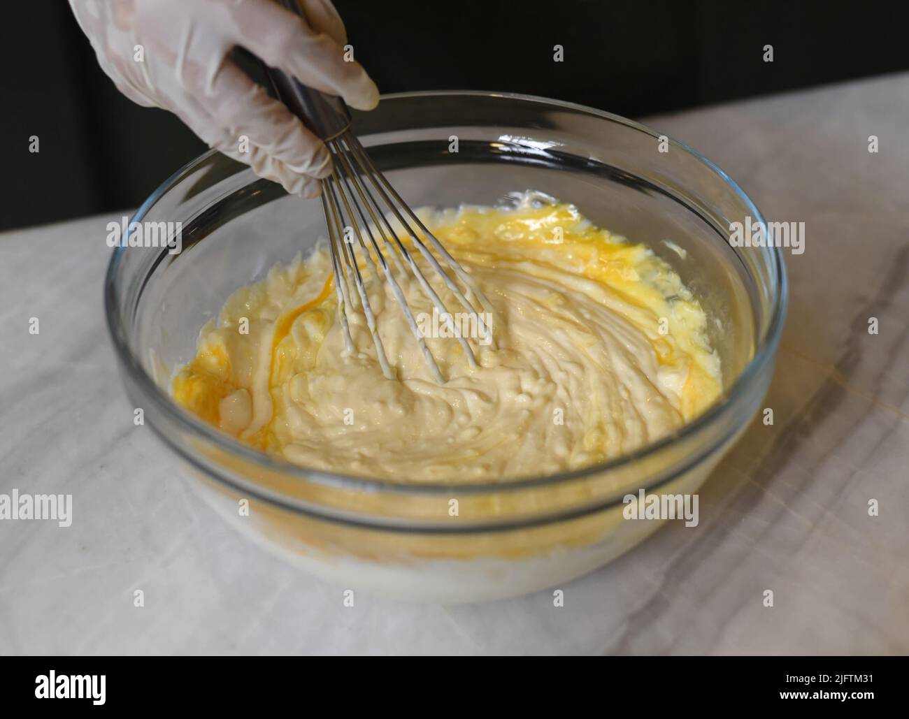 A hand in rubber glove stirring dough for a cake Stock Photo
