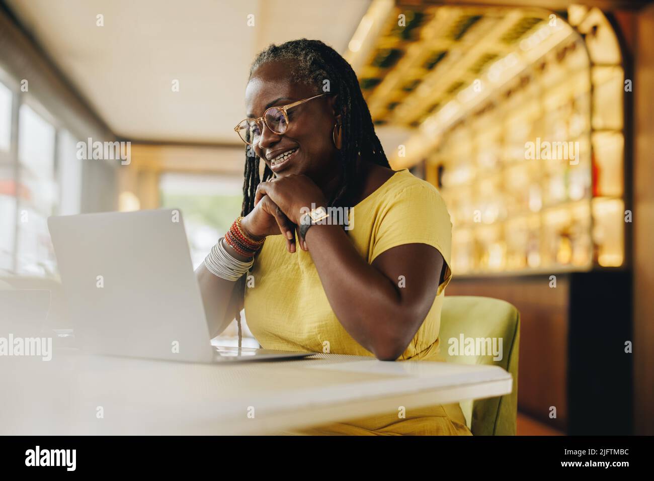 Black businesswoman having a video call with her colleagues while working in a cafe. Mature businesswoman with dreadlocks attending a virtual meeting Stock Photo