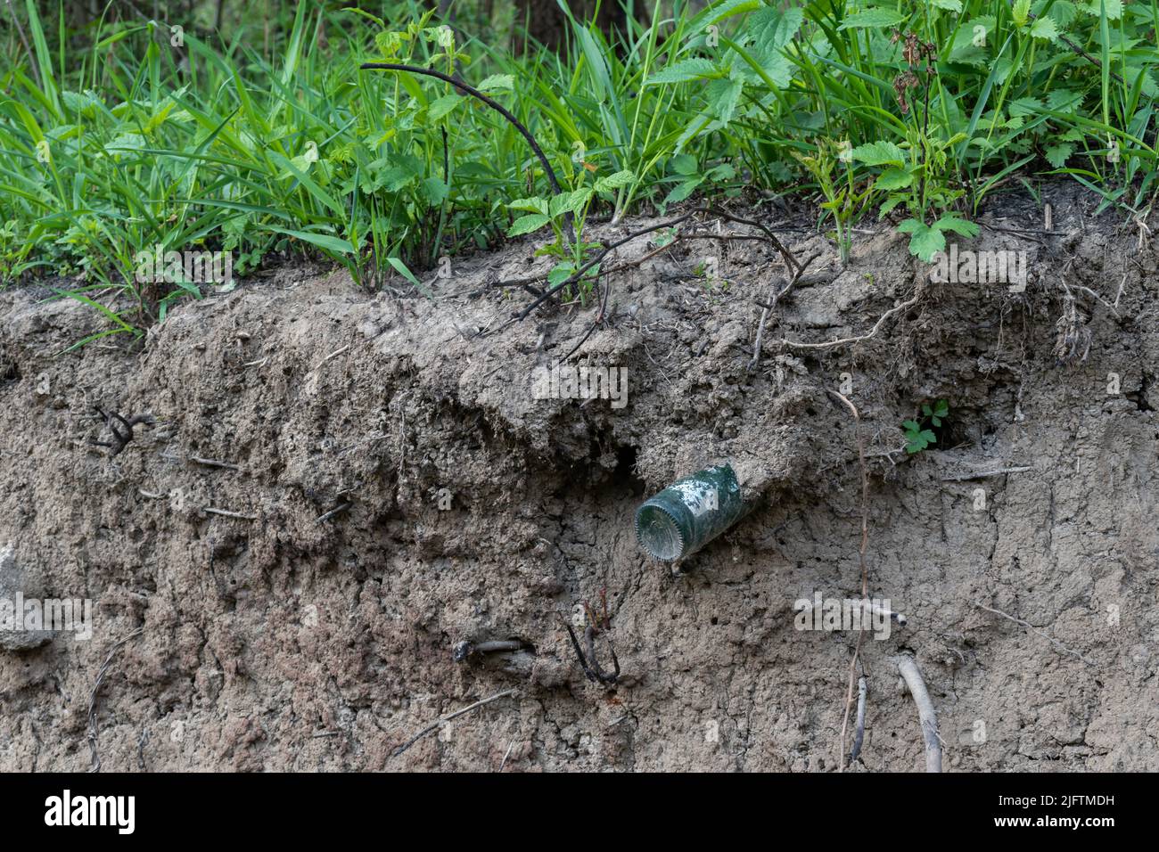 Glass bottle under layer of earth in washed out riverbank, glass pollution, reckless waste disposal Stock Photo