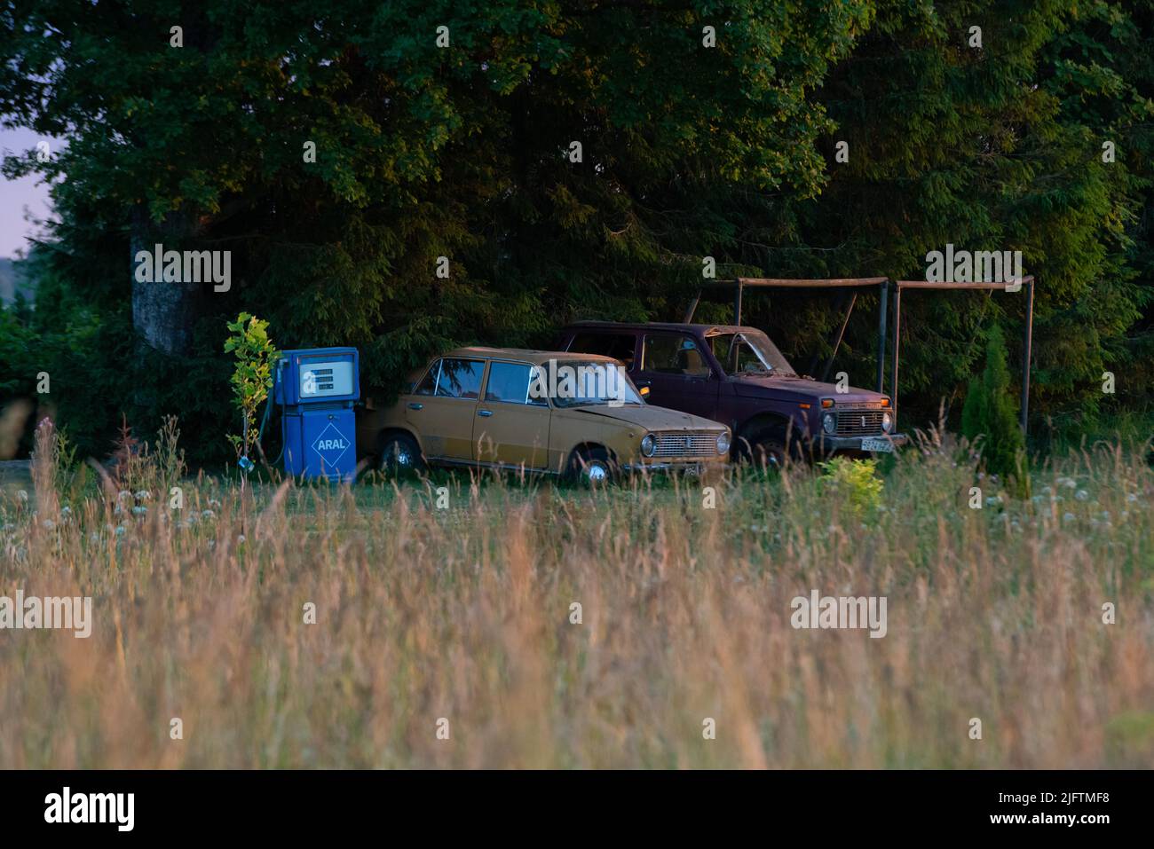 Old Russian cars stand on the edge of a cornfield under the warm summer sunset. Next to them is the refueling tank. Stock Photo