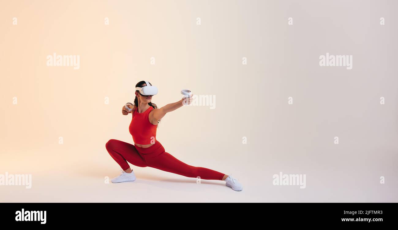 Active young woman working out in virtual reality. Sporty young woman doing fitness exercises using a pair of gaming controllers. Athletic young woman Stock Photo