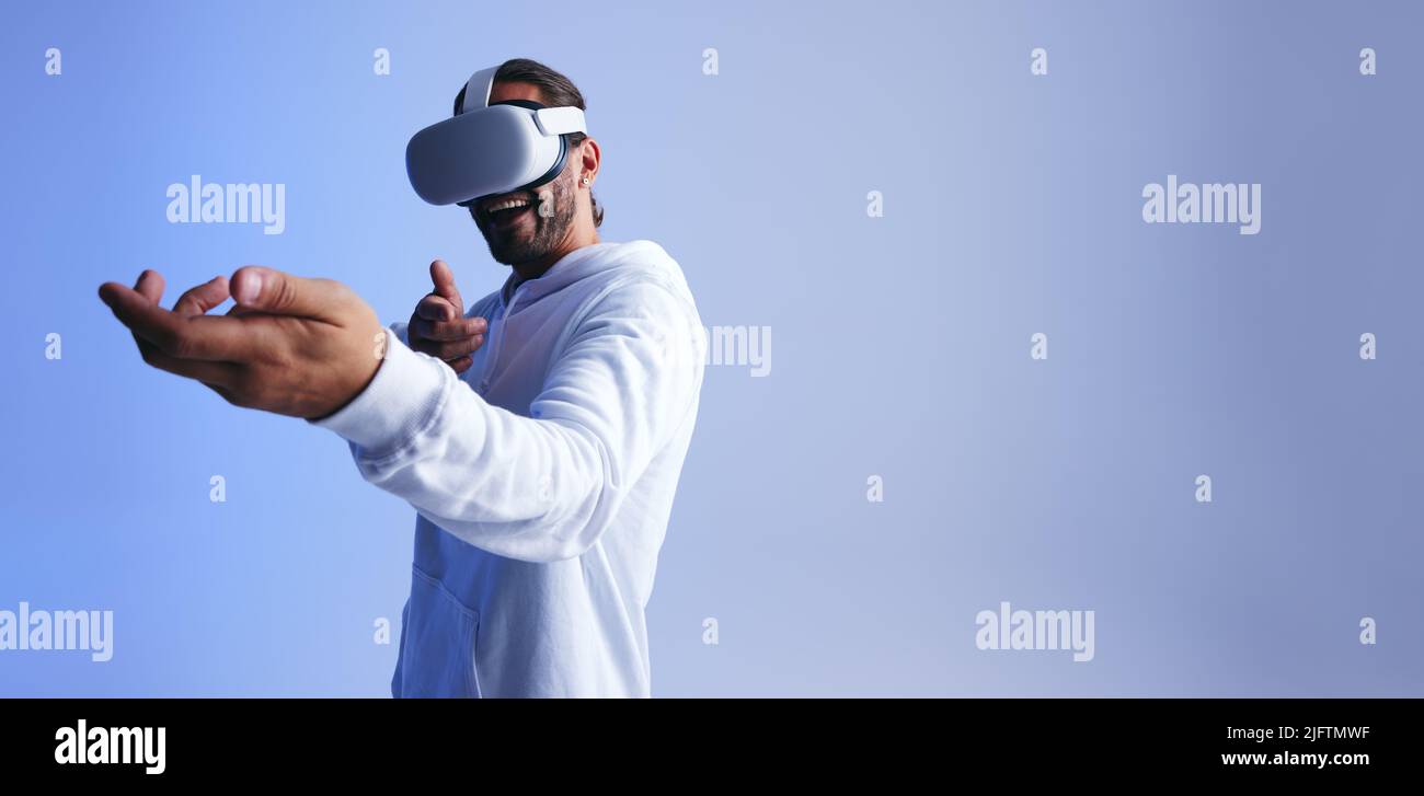 Cheerful young man shooting with his hands in a virtual reality game. Happy young man smiling while wearing a virtual reality headset. Young man havin Stock Photo