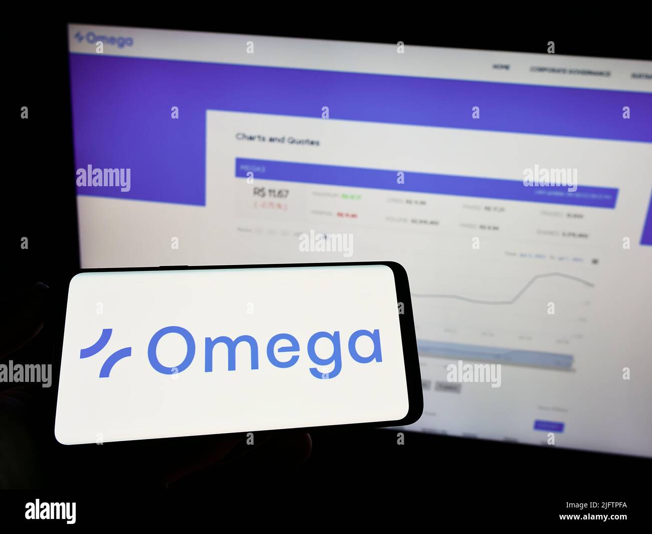 Person holding mobile phone with logo of Brazilian renewable energy company Omega Energia on screen in front of web page. Focus on phone display. Stock Photo