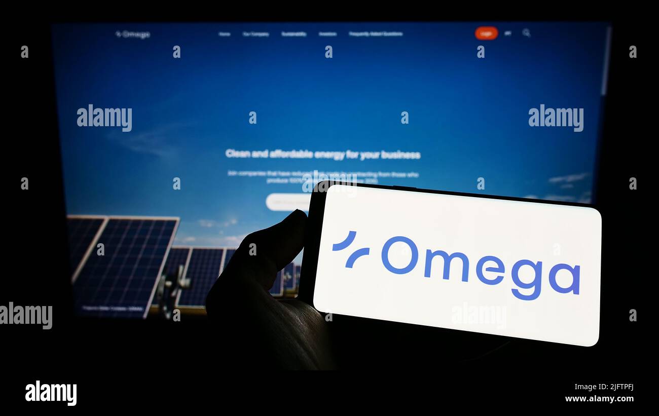 Person holding smartphone with logo of Brazilian renewable energy company Omega Energia on screen in front of website. Focus on phone display. Stock Photo