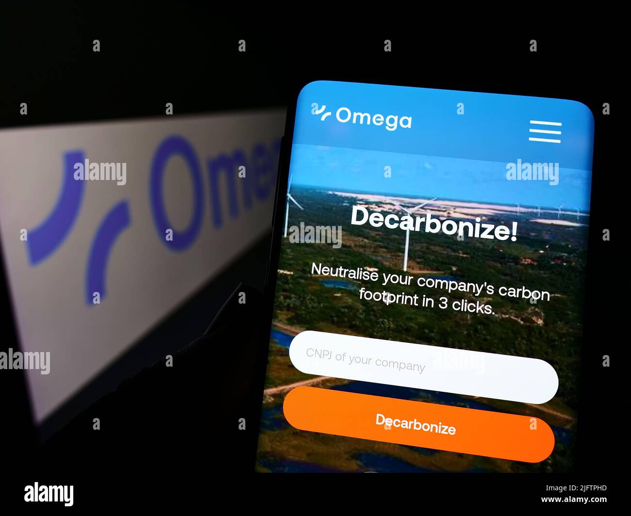 Person holding smartphone with website of Brazilian renewable energy company Omega Energia on screen with logo. Focus on center of phone display. Stock Photo