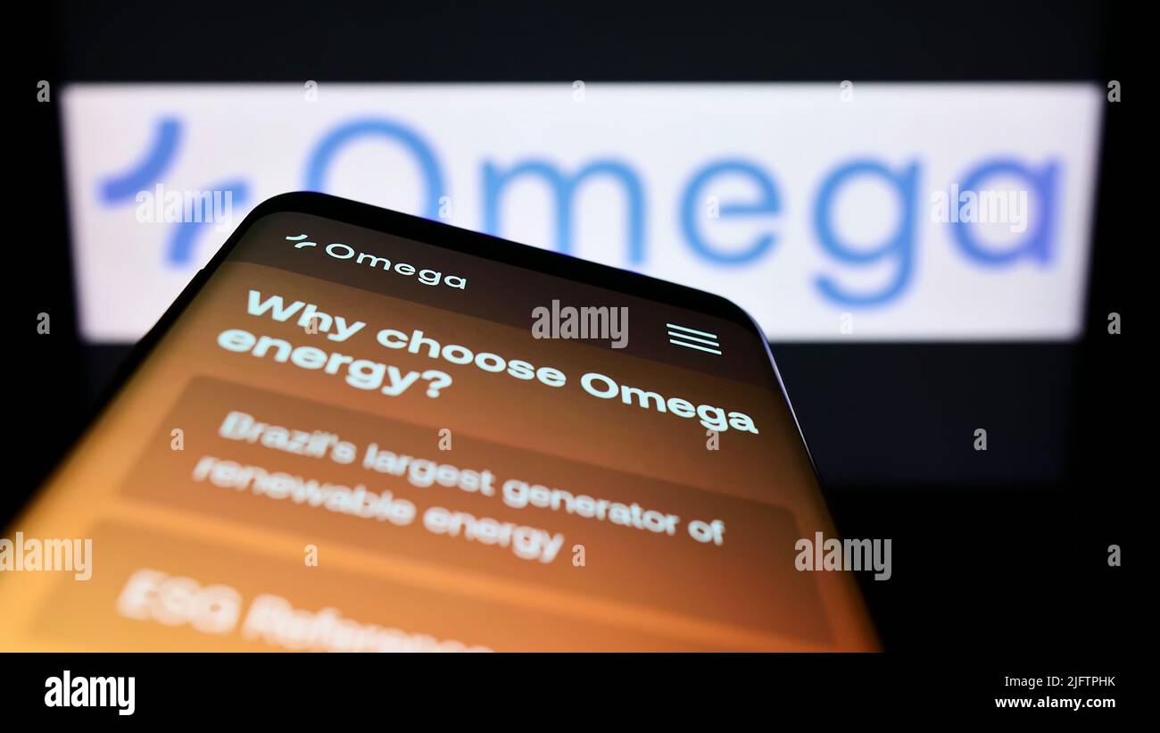 Mobile phone with webpage of Brazilian renewable energy company Omega Energia on screen in front of logo. Focus on top-left of phone display. Stock Photo