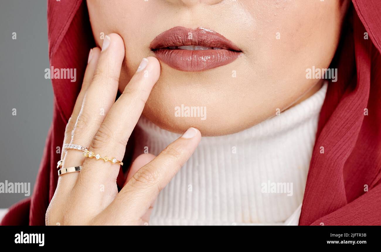 Muslim woman wearing rings, lipstick, a hijab, touching her face and posing in studio. Closeup of half headshot of a confident arab model isolated Stock Photo