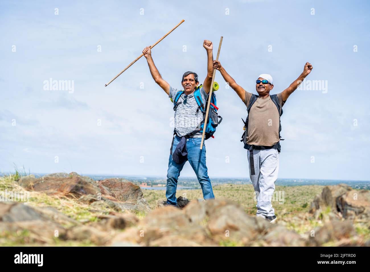 Happy friends celebration by raising hands with stick after reaching destination on hill - concept of outdoor entertainment activities, trekking and Stock Photo