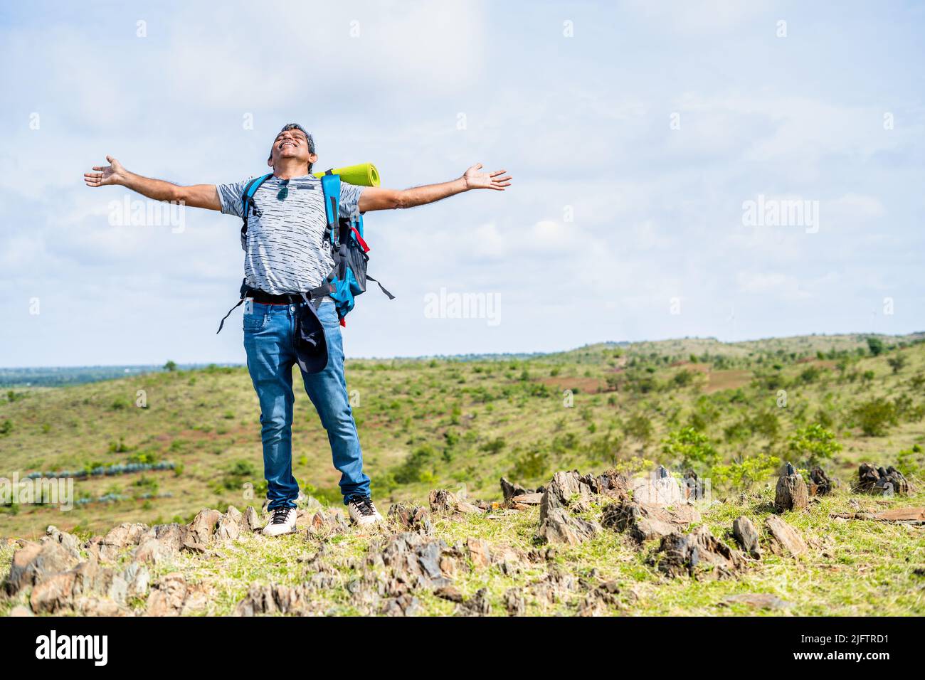 Middle aged man feeling or admiring natures fresh air by stretching arms during hiking at hill top - concept of refreshment, active healthy lifestyle Stock Photo