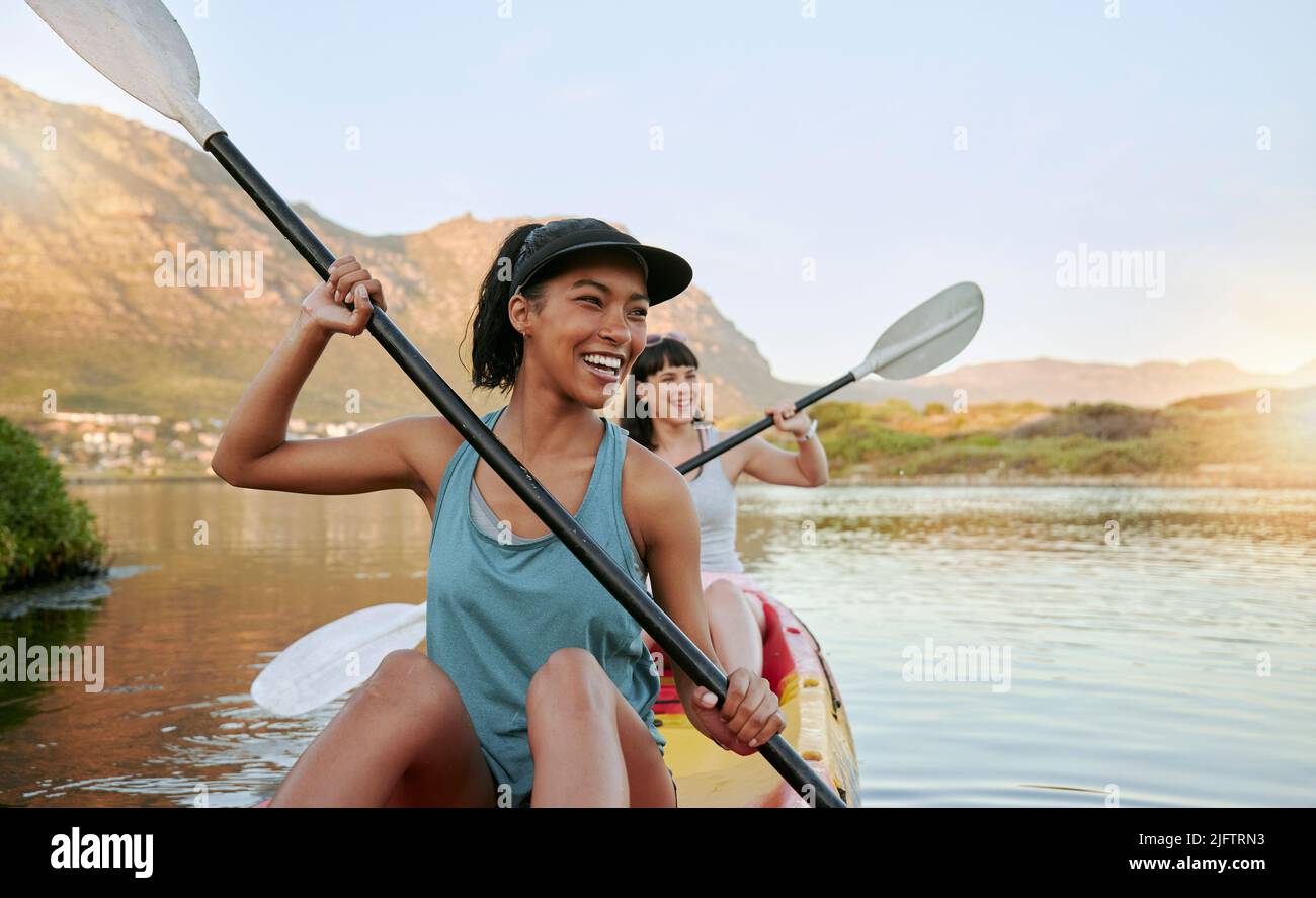 Two smiling friends kayaking on a lake together during summer break. Smiling and happy playful women bonding outside in nature with water activity Stock Photo