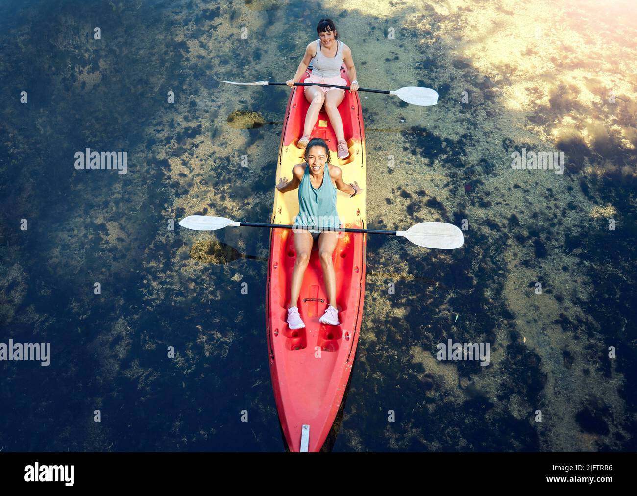 Above view of two smiling friends kayaking on the ocean together over summer break. Portrait of happy women canoeing and bonding outside in nature Stock Photo