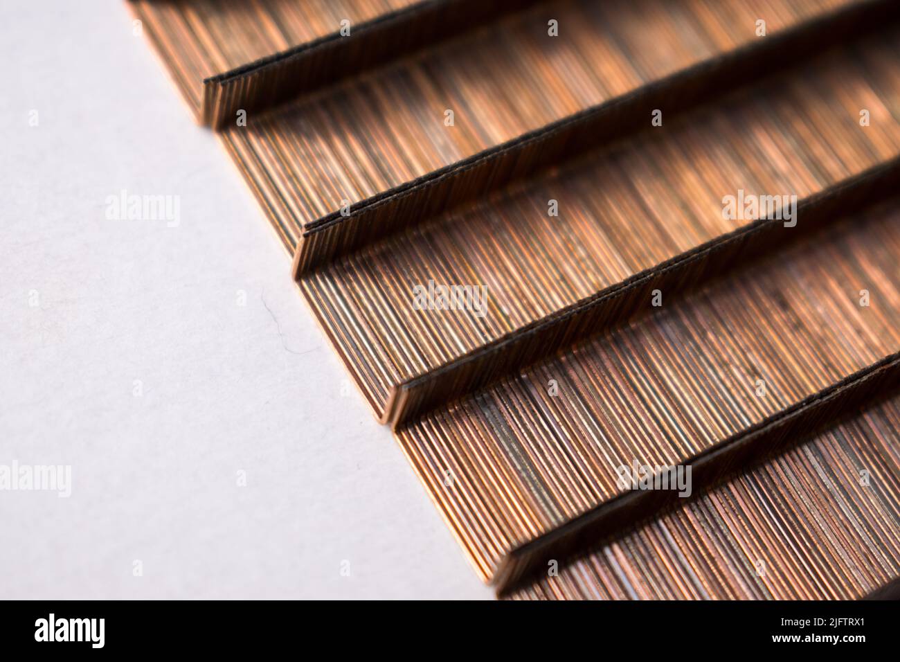 A top view of row of upside-down bronze stapler pins on white table ...