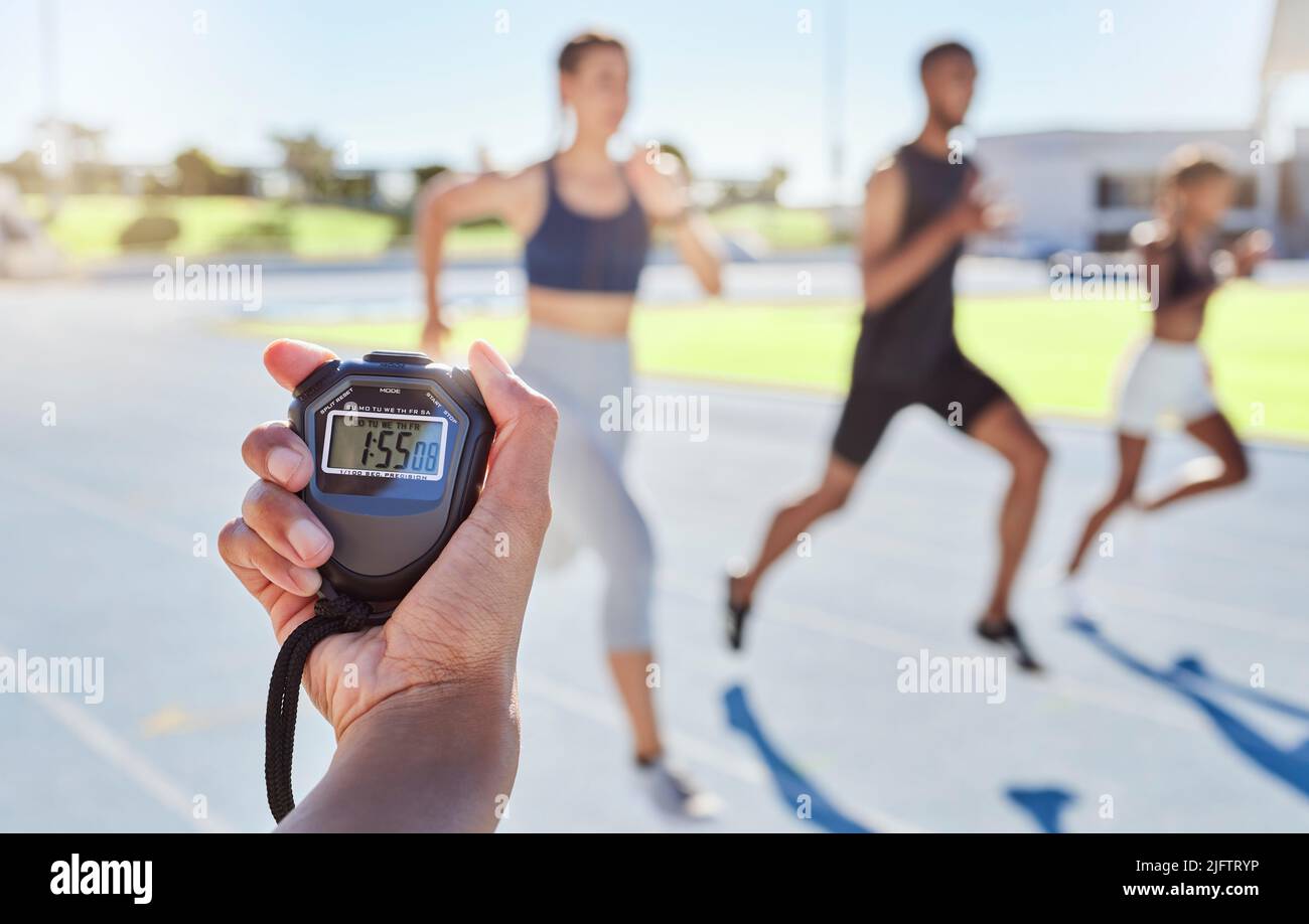 A sport coach timing athletes progress using a stopwatch. .Blurred athletes racing towards finish line and breaking the record. Stopwatch measuring Stock Photo