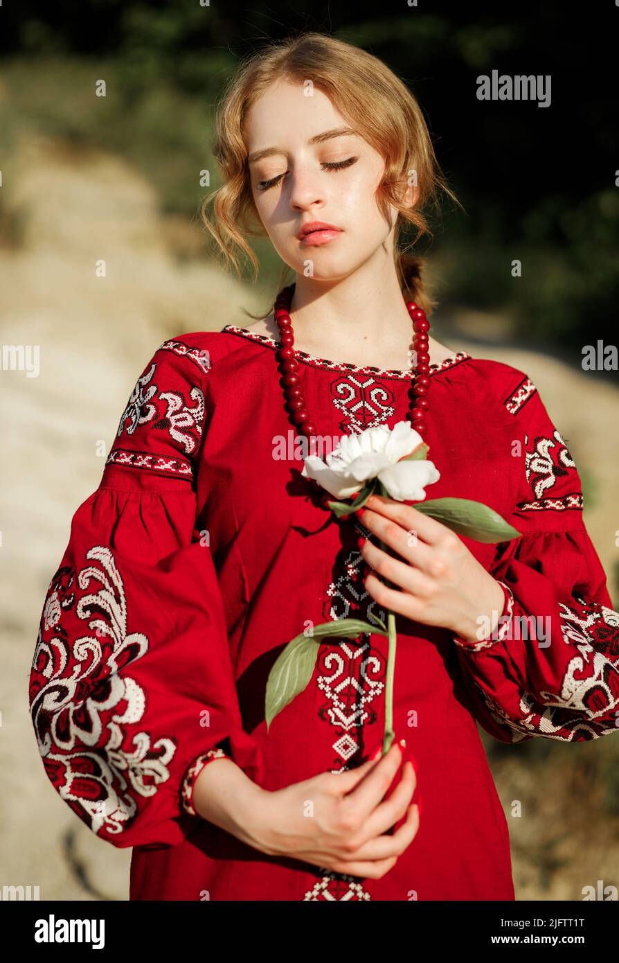 A beautiful girl in a traditional ethnic red dress posing outdoors with a white peony flower in her hand Stock Photo