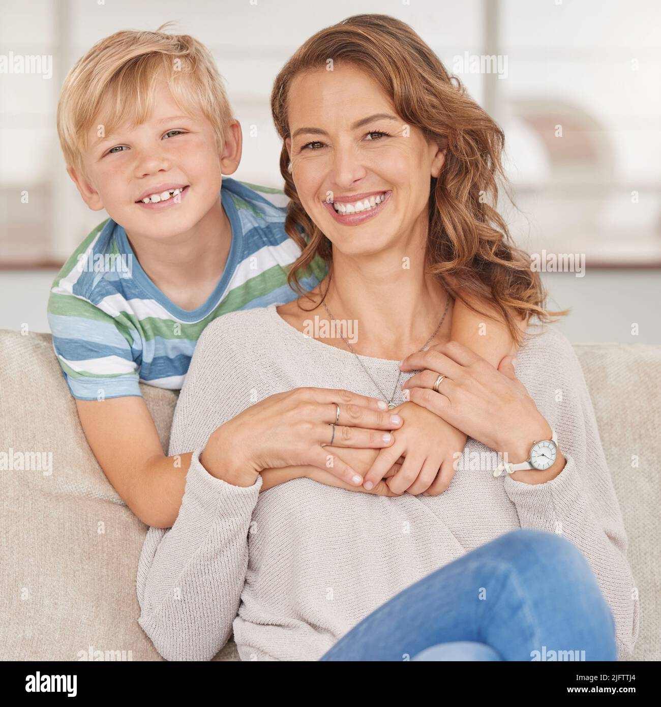 Portrait of a single mother and her son. Adorable boy bonding with his single parent and hugging her in the living room at home. Smiling woman and her Stock Photo