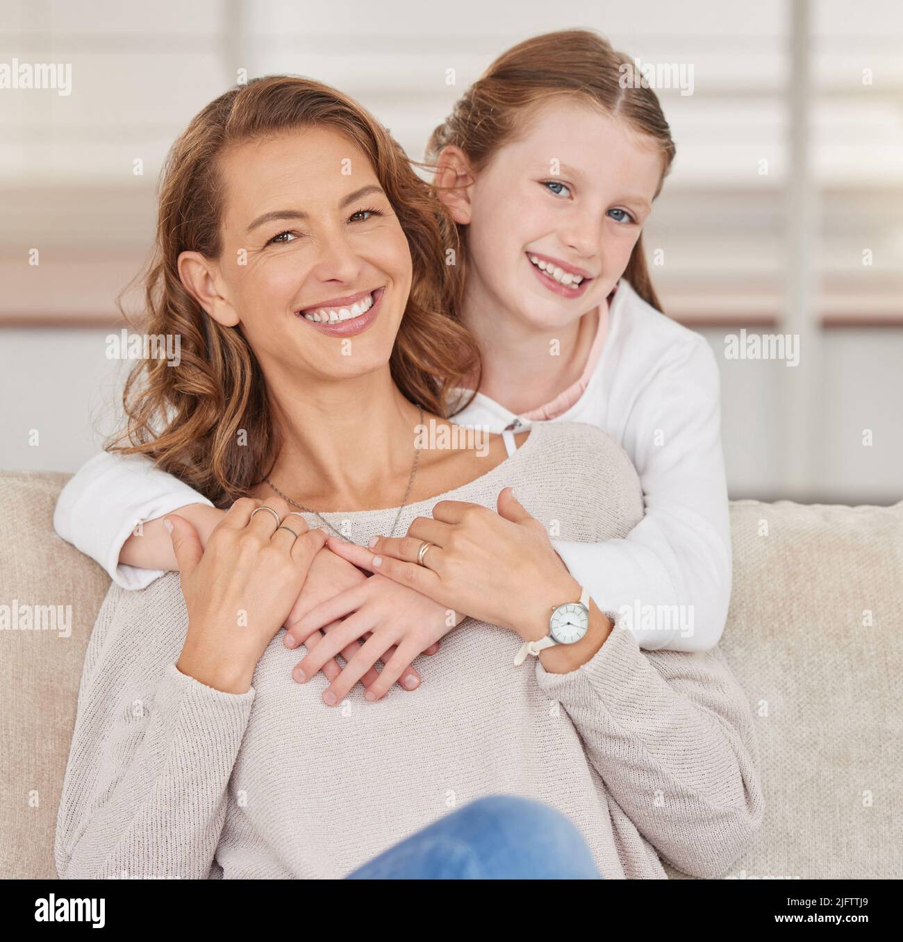 Portrait of a single mother and her daughter. Adorable girl bonding with her single parent and hugging in the living room at home. Smiling woman and Stock Photo