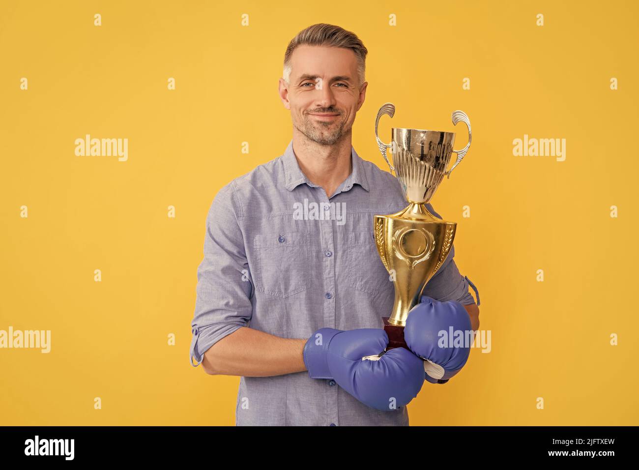 smiling adult man in boxing gloves hold golden cup on yellow background, victory Stock Photo