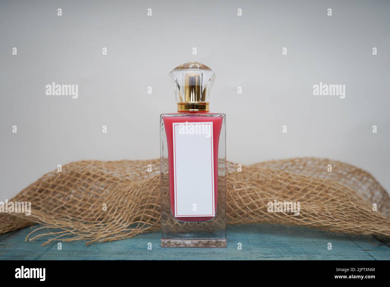 Red Perfume bottle and cap for branding isolated on white background with green table and burlap, Red Perfume bottle mockup. Stock Photo