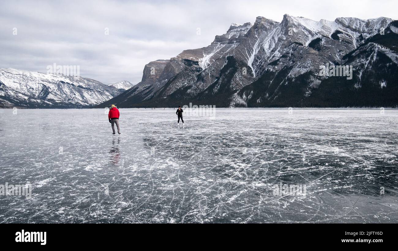 Couple wild skating on a frozen alpine lake under a big mountain , Banff N. Park, Canada Stock Photo